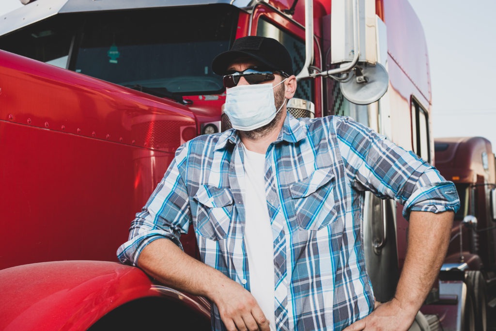 Image: A trucker wearing a mask, leaning against a red truck. View resources for truckers here.