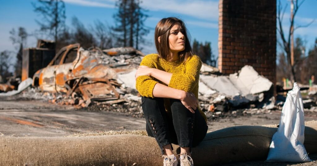 Woman sitting outside after her car was damaged due to a natural disaster.