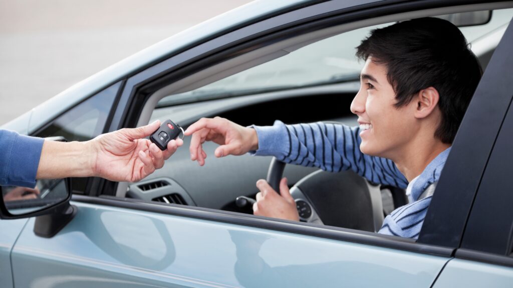 Excited teen driver sitting in the driver's seat as parents review auto insurance for teen drivers before summer.